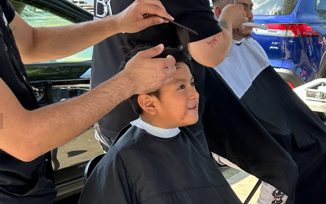 A hairstylist works on a child’s haircut outdoors