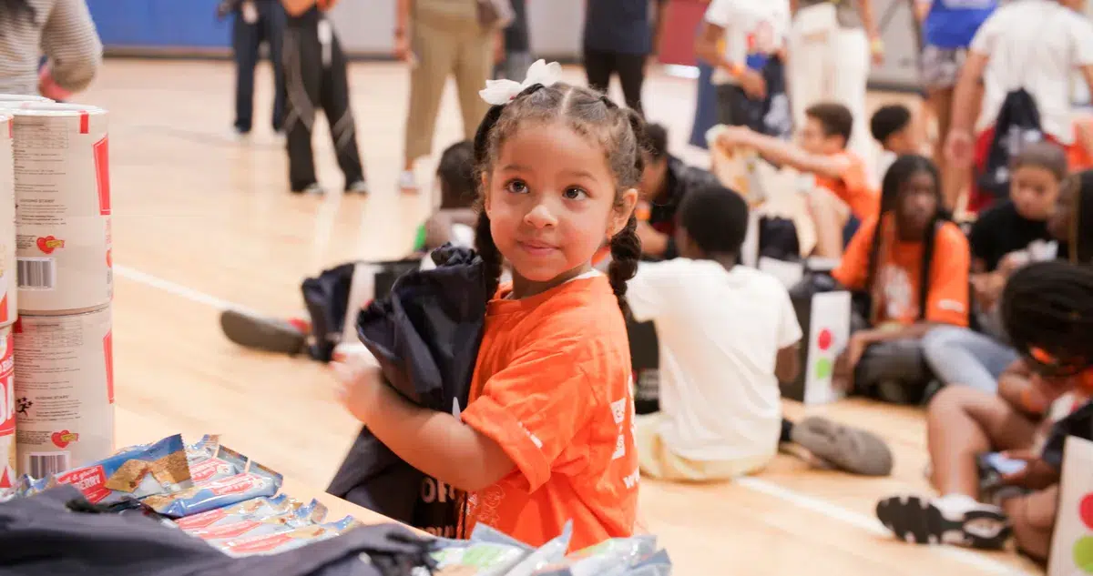 Little girl smiles while holding a bag full of fresh fruit and shelf-stable goods at a Food Bank For NYC distribution.