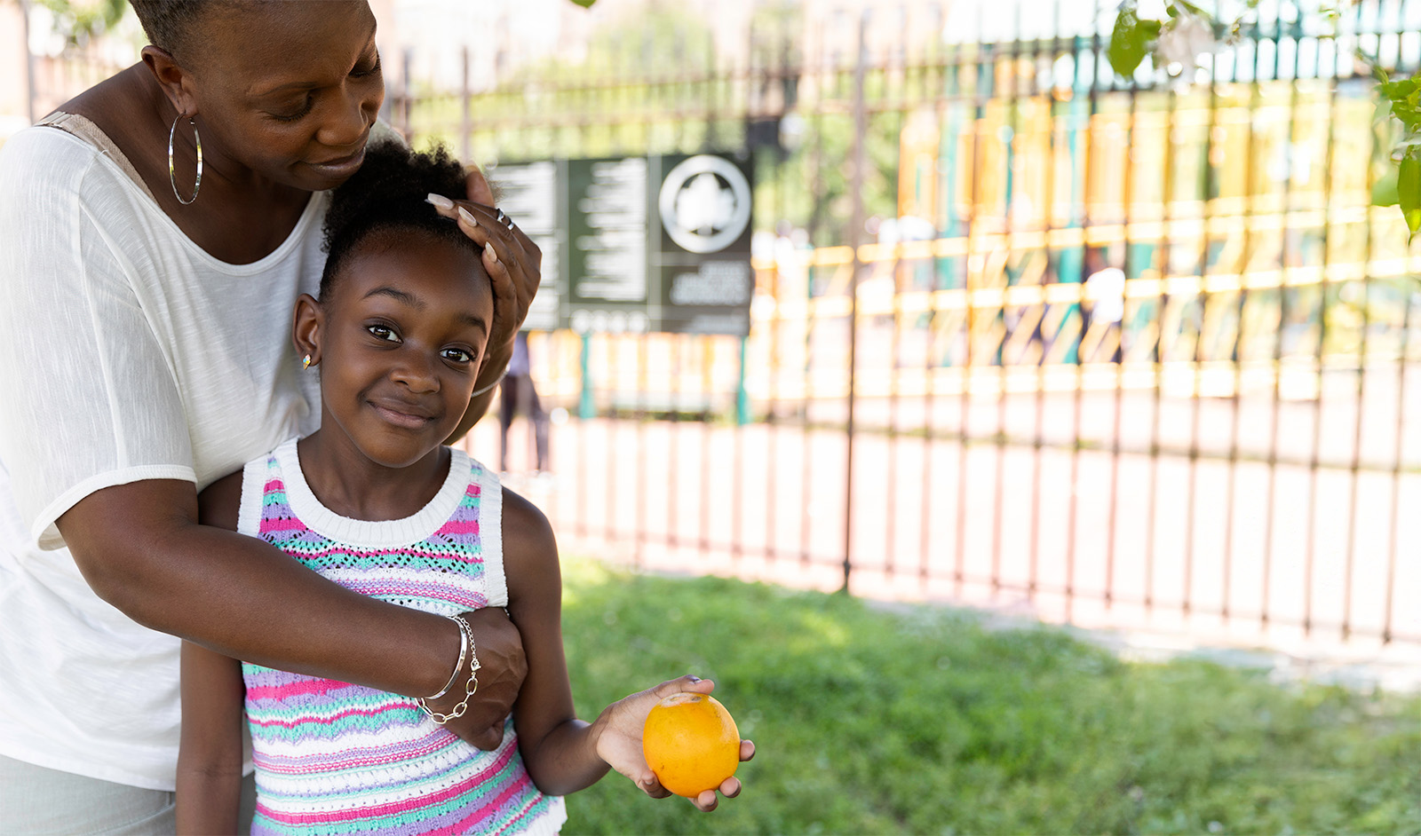 Mother hugging child holding an orange left on screen