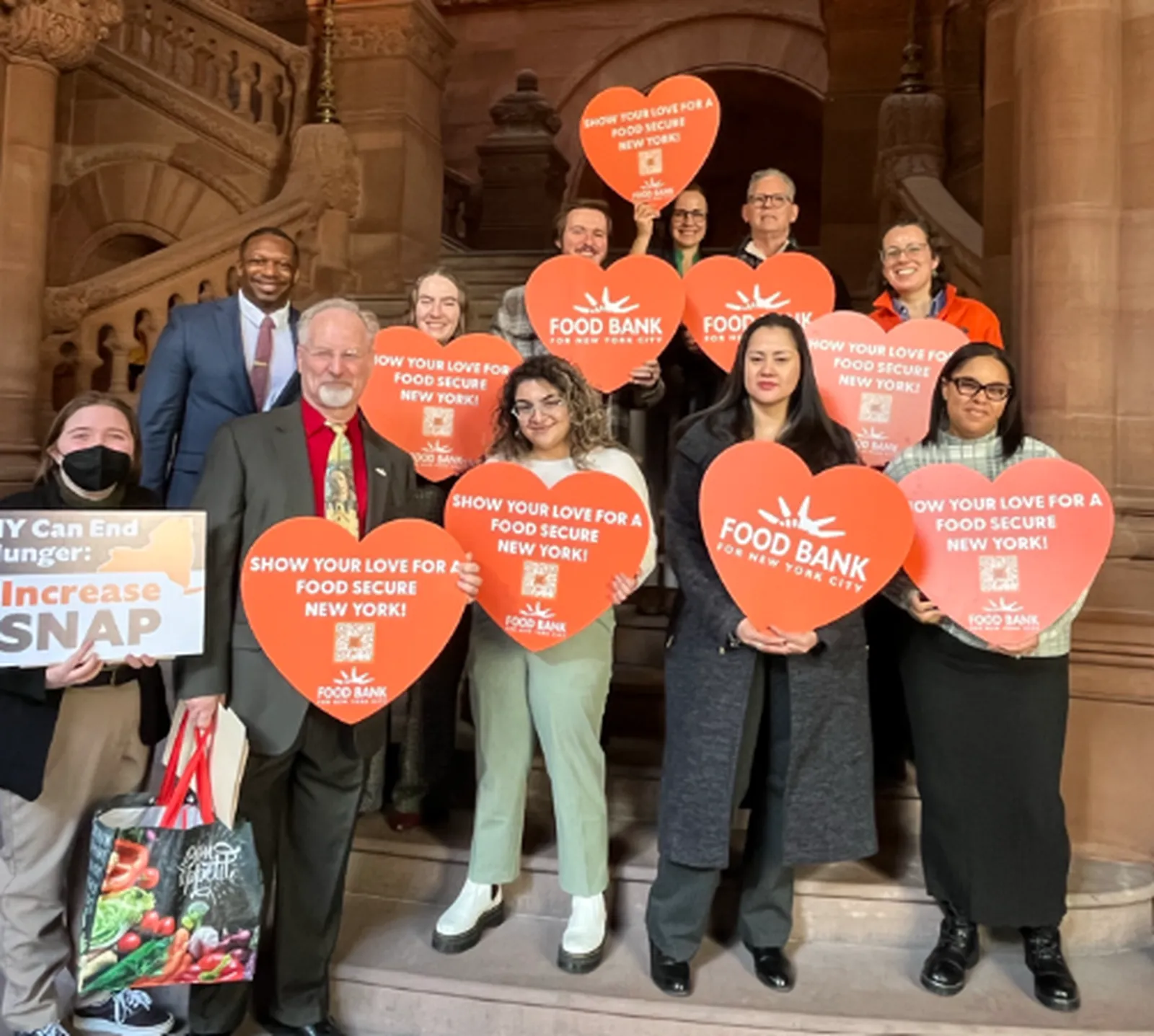 become-an-advocate-state-budget_result Group of people standing on a staircase holding heart-shaped Food Bank for NYC signs and a poster advocating for increased SNAP benefits.