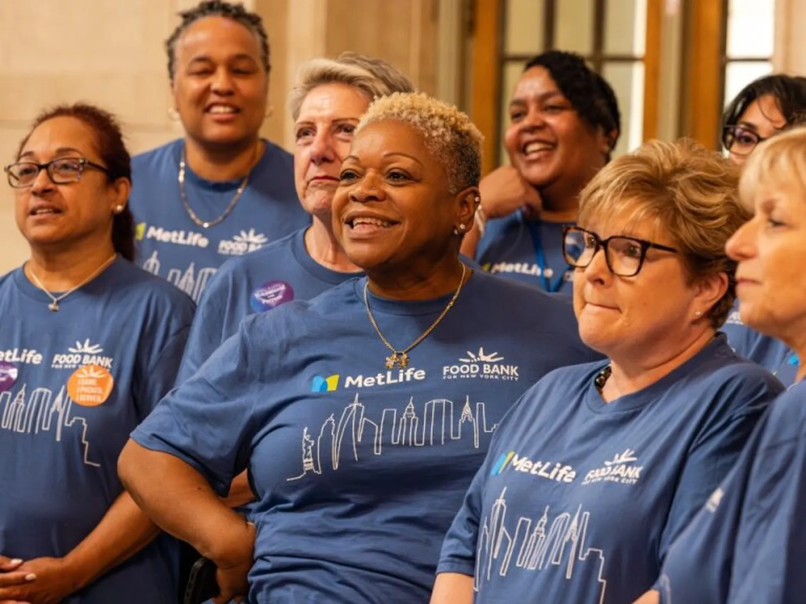 Group of employees in blue Food Bank for NYC shirts standing together indoors.