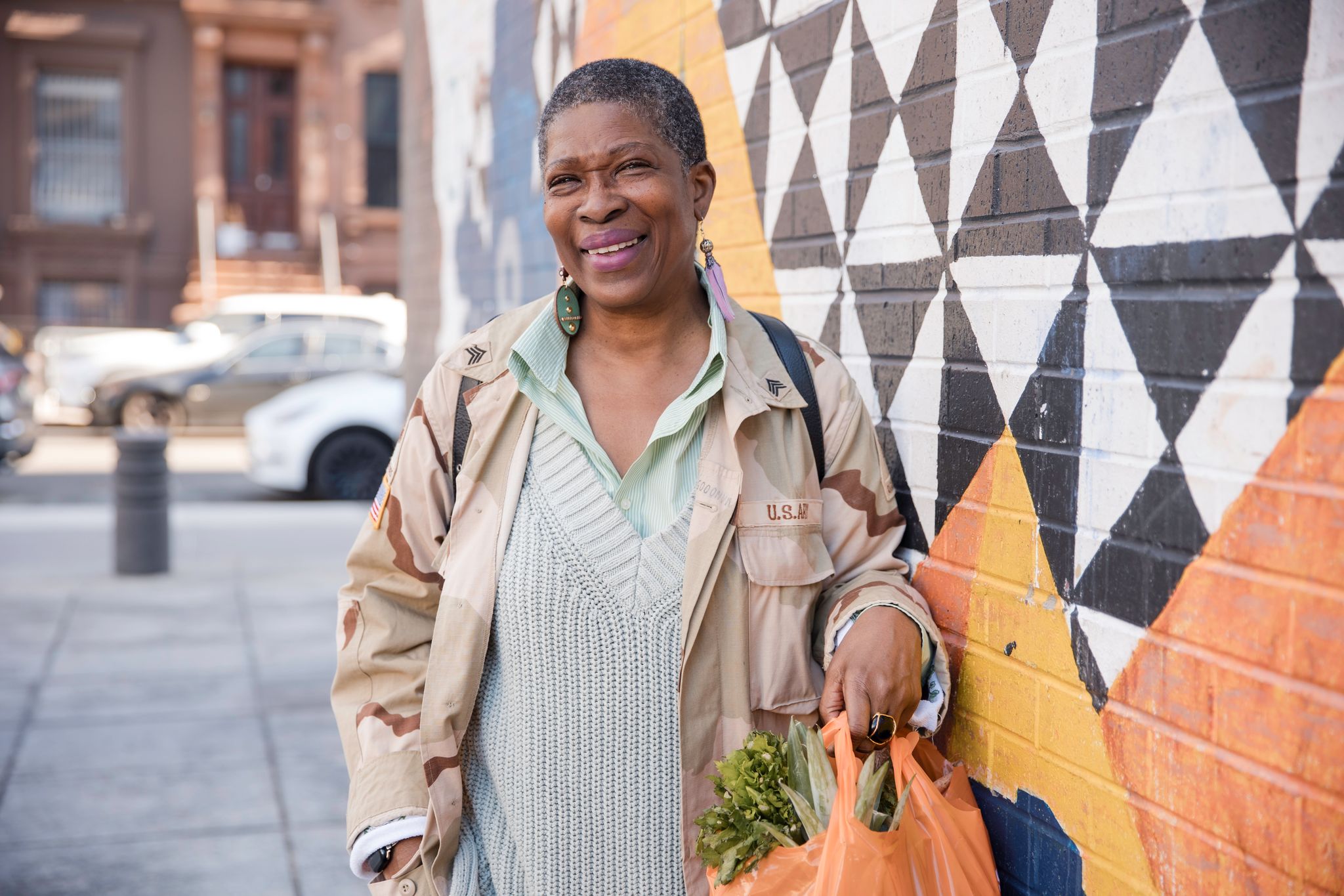 Smiling woman with groceries standing by colorful mural.