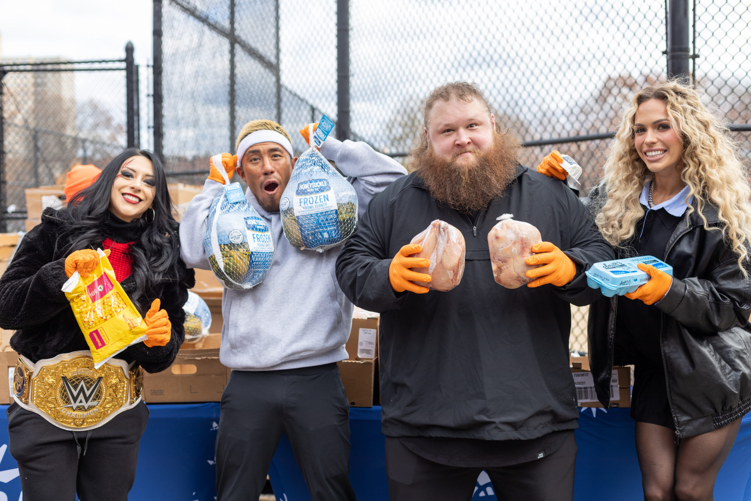 WWE Superstars Maxxine Dupri, Otis, Akira Tozawa, and Stephanie Vaquer smile while holding bags of fresh produce and turkey meat at Food Bank For NYC's mobile pantry.