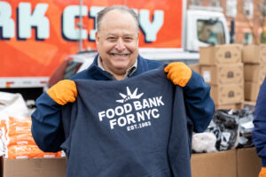 David Unger, President of the National Mah Jongg League, holds up a dark navy Food Bank For NYC hoodie before volunteering at a mobile pantry.