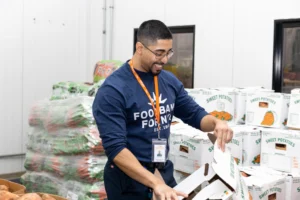 Food Bank For NYC Volunteer smiles while packing a box of sweet potatoes for TSA workers.